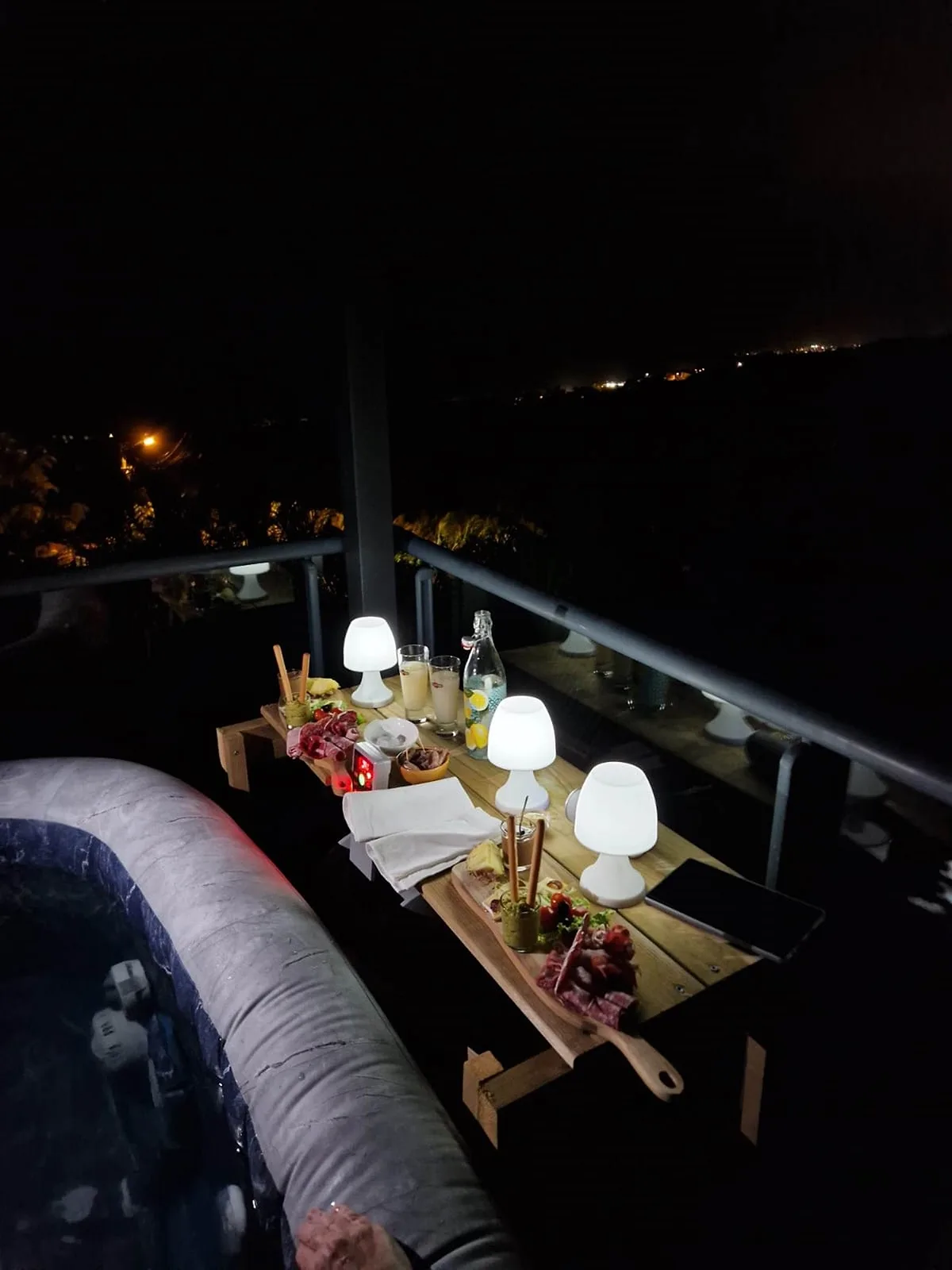 Un plateau d'apéritif éclairé de petites lampes sur la terrasse, de nuit, à côté du spa