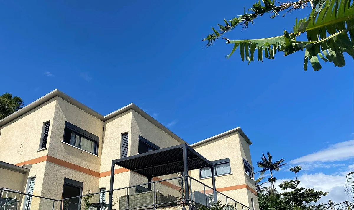 La façade de la villa, ses grandes baies noires et la pergola de la terrasse