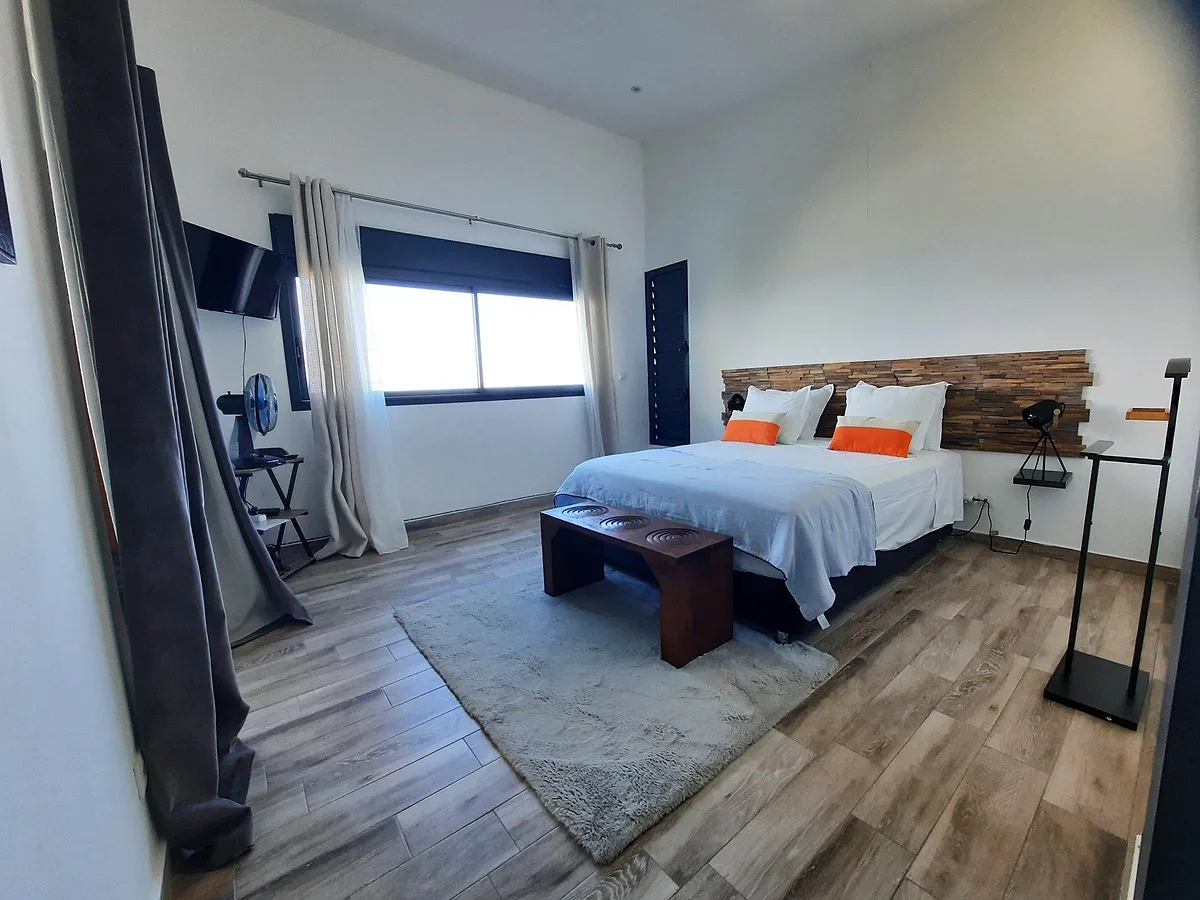 La Géranium, coussins orange et banc en bois au pied du lit