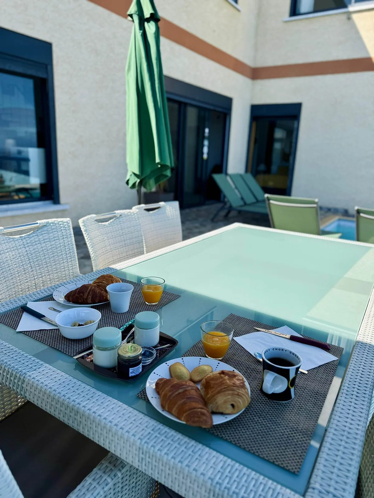 Le petit déjeuner dressé sur la table de verre de la terrasse, près de la piscine
