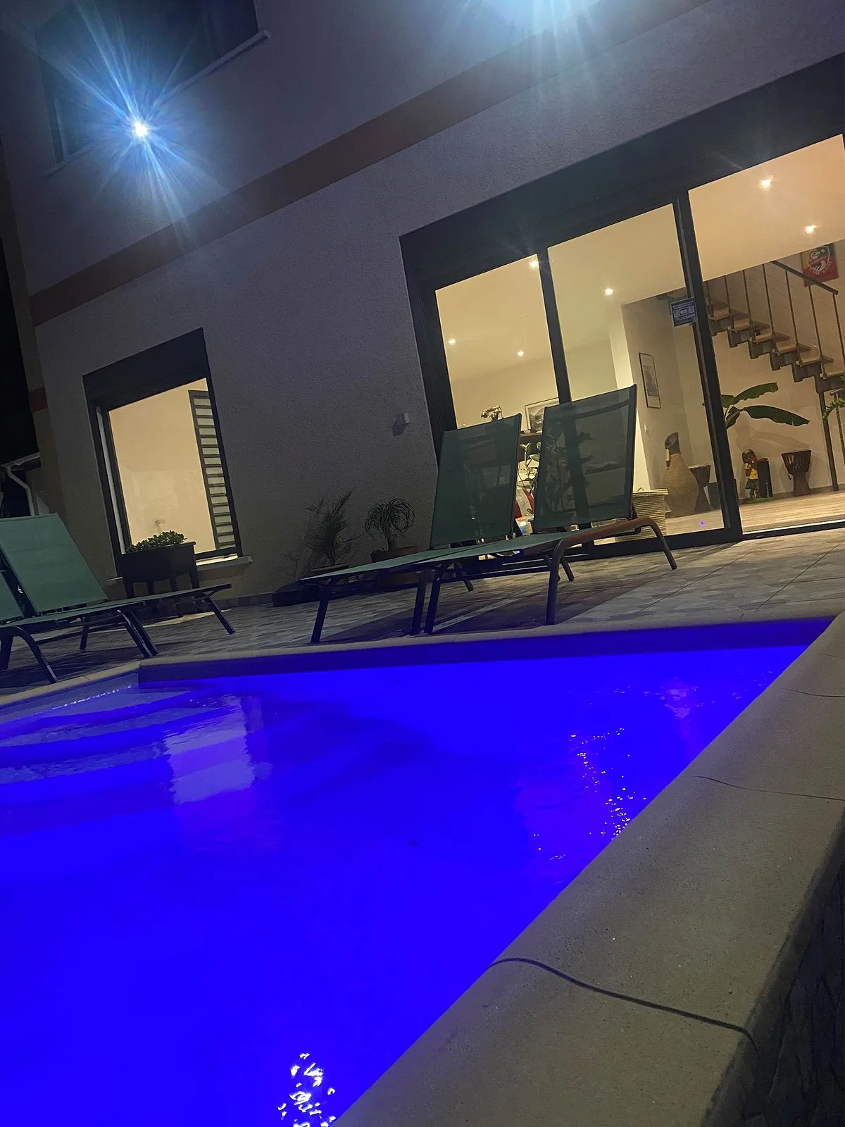La piscine éclairée en bleu, de nuit, devant les baies de la villa
