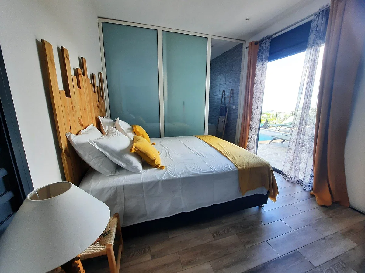 La chambre Victoria, son lit à la tête de lit en bois et la baie ouverte sur la terrasse